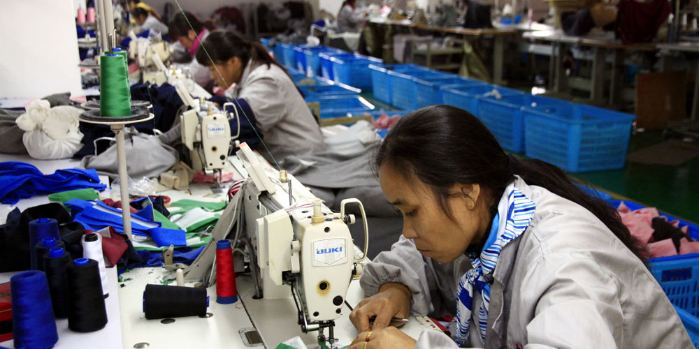 Women working behind their sewing machines in a large factory.